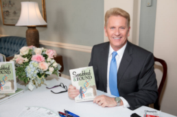 Frank Billingsley holding his book Swabbed & Found at a signing table, highlighting his adoption story and DNA genealogy journey.