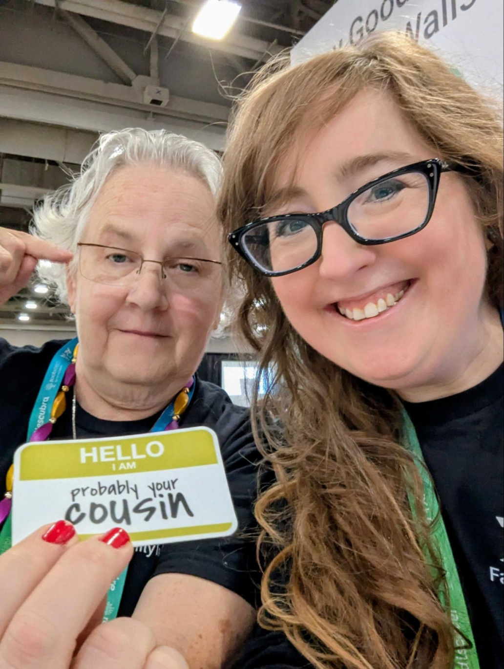 Katy Rowe-Schurwanz and Mags Gaulden holding a “probably your cousin” badge at a genealogy conference.
